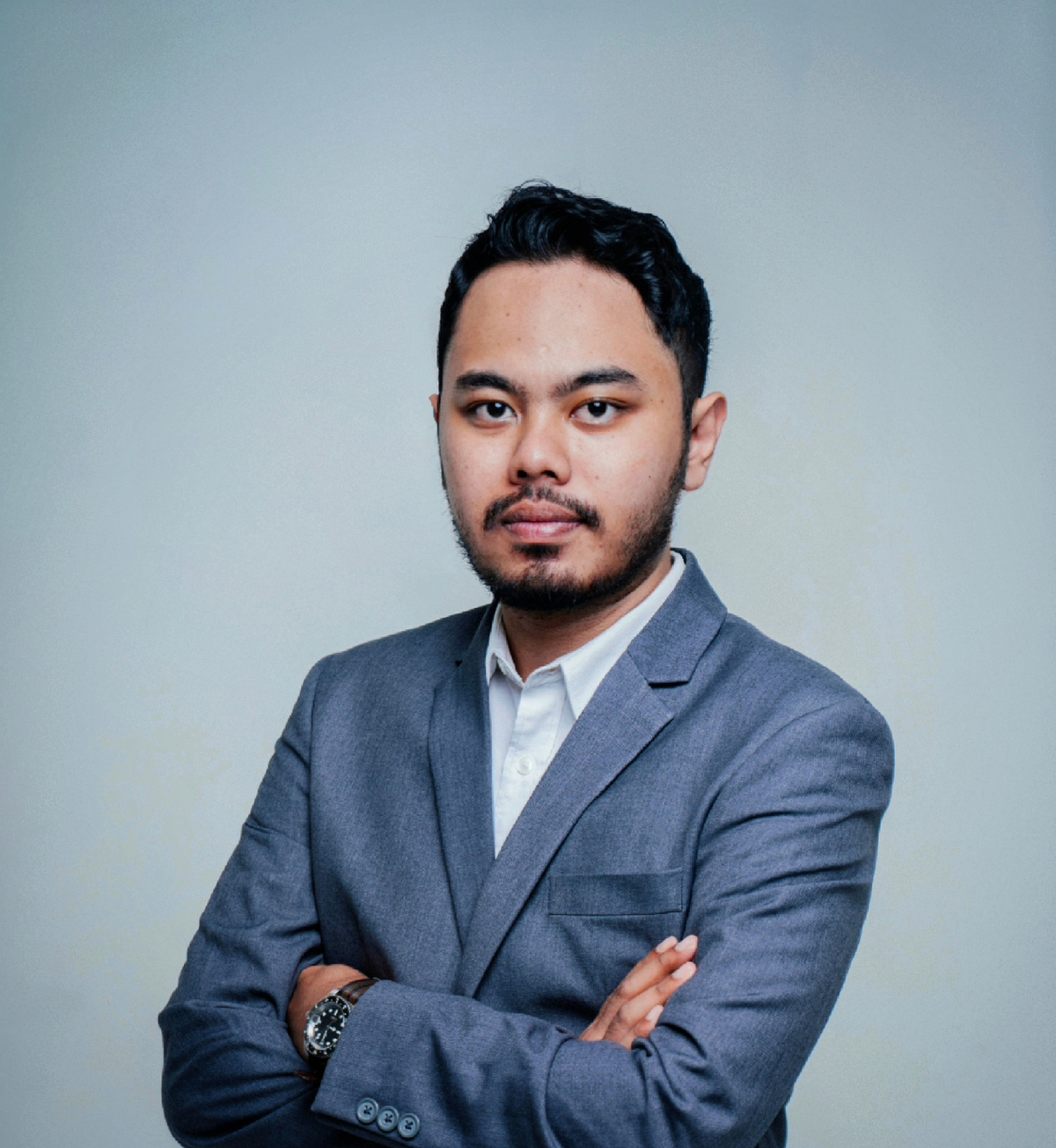 A professional man with short hair, wearing a suit and tie, standing confidently.